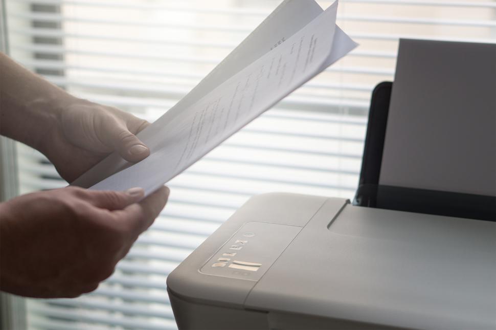Free Image of Hands holding printed sheets over a printer 