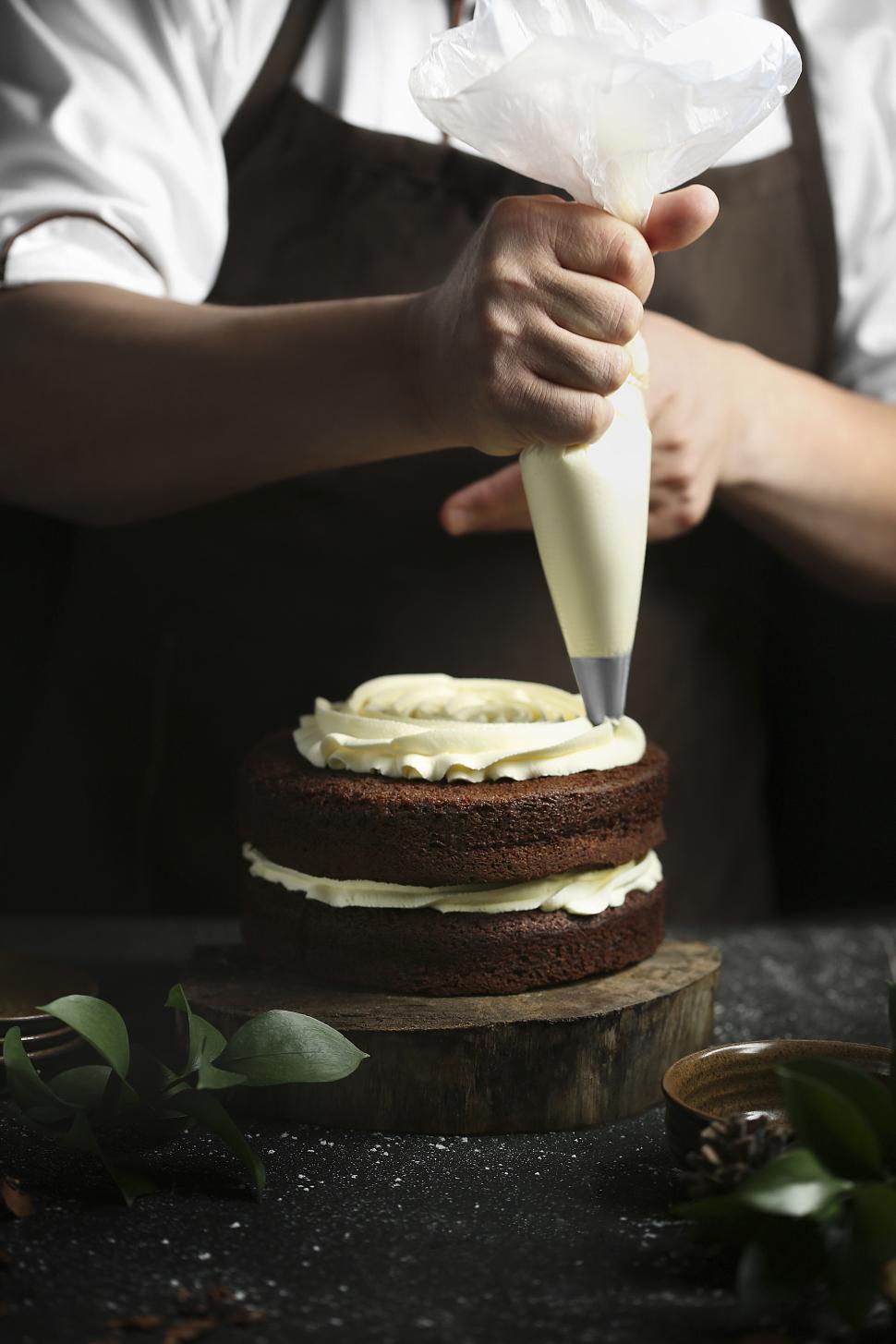 Free Image of Piping white cream onto chocolate cake with piping bag 