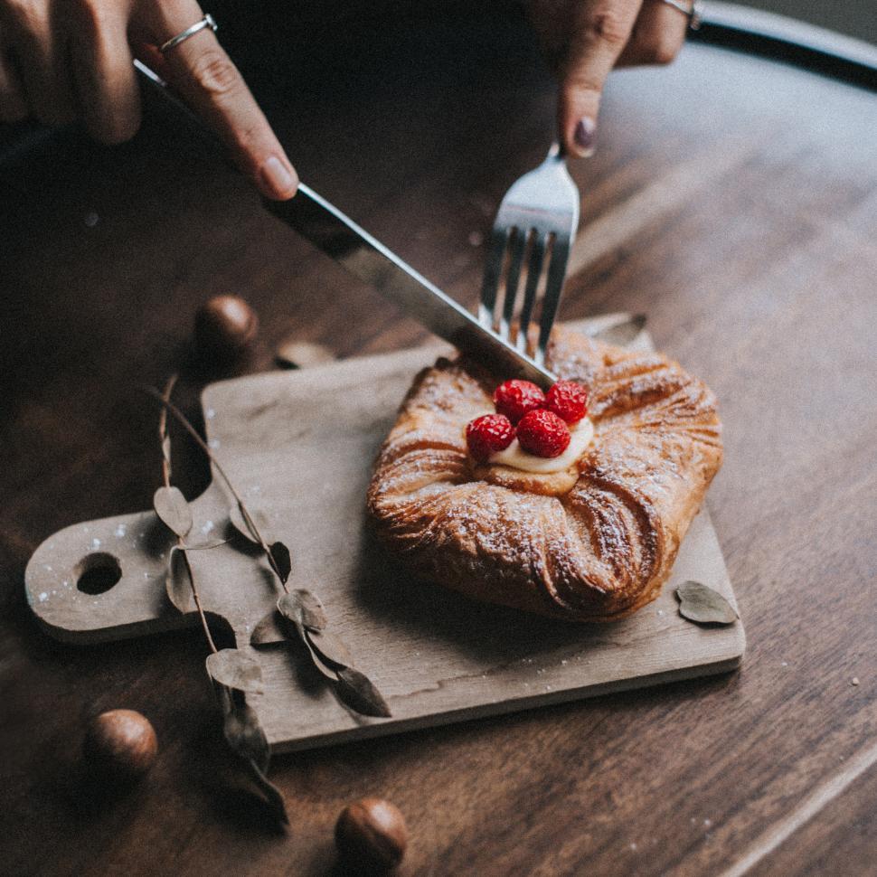 Free Image of Cutting danish pastry with fork and knife on wooden plate 