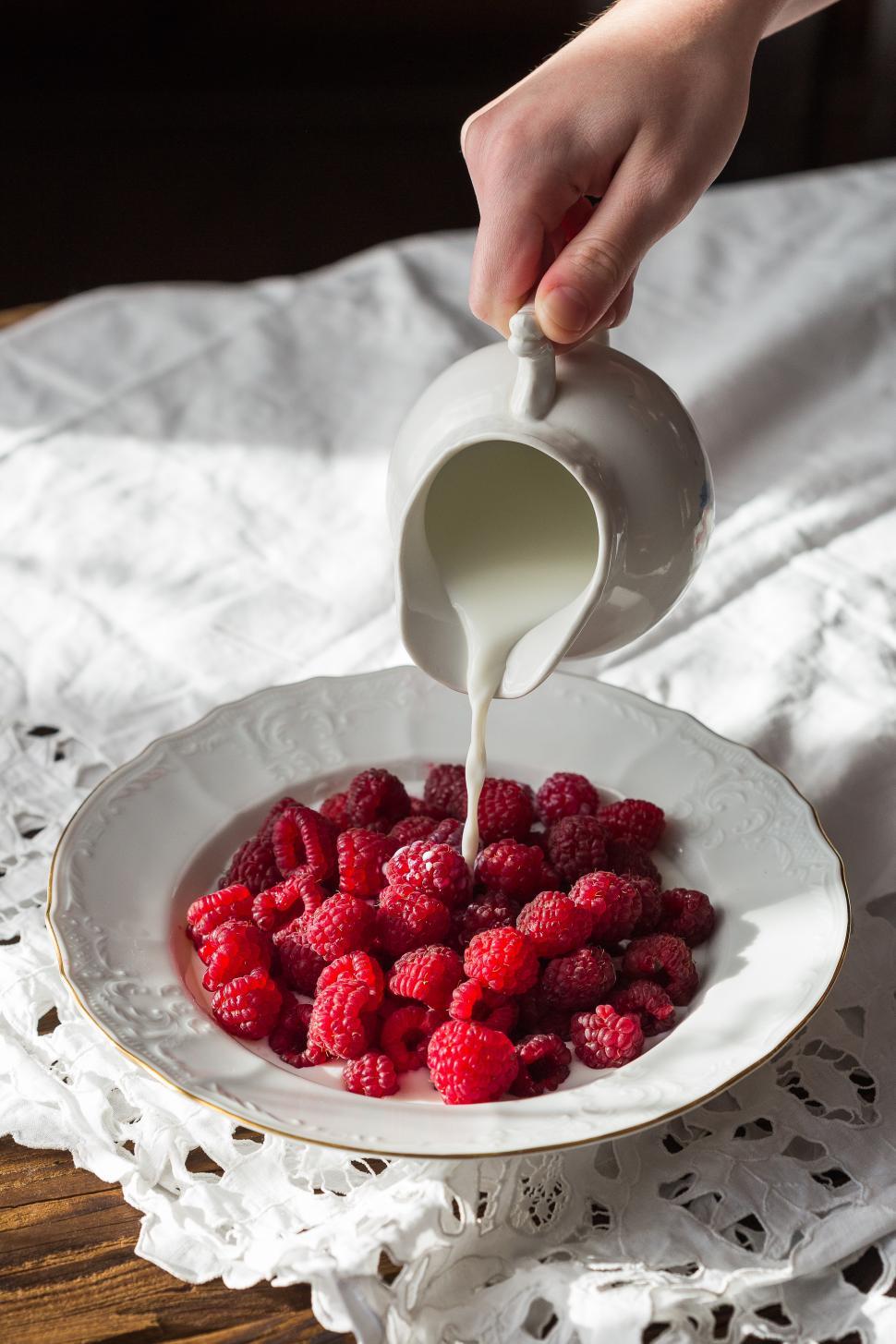 Free Image of Close up milk being poured into a plate full of raspberries 