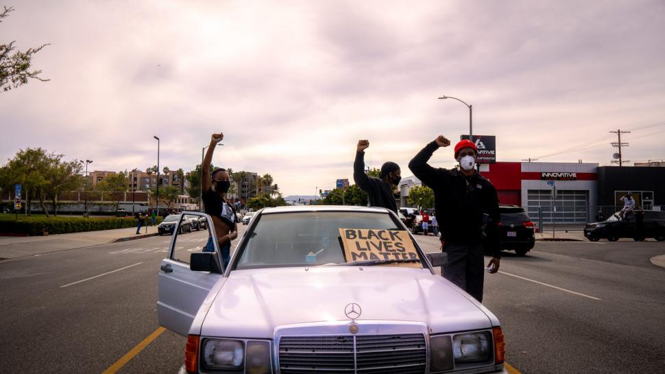 Free Image of Men outside a car with fists raised and Black Lives Matter sign 