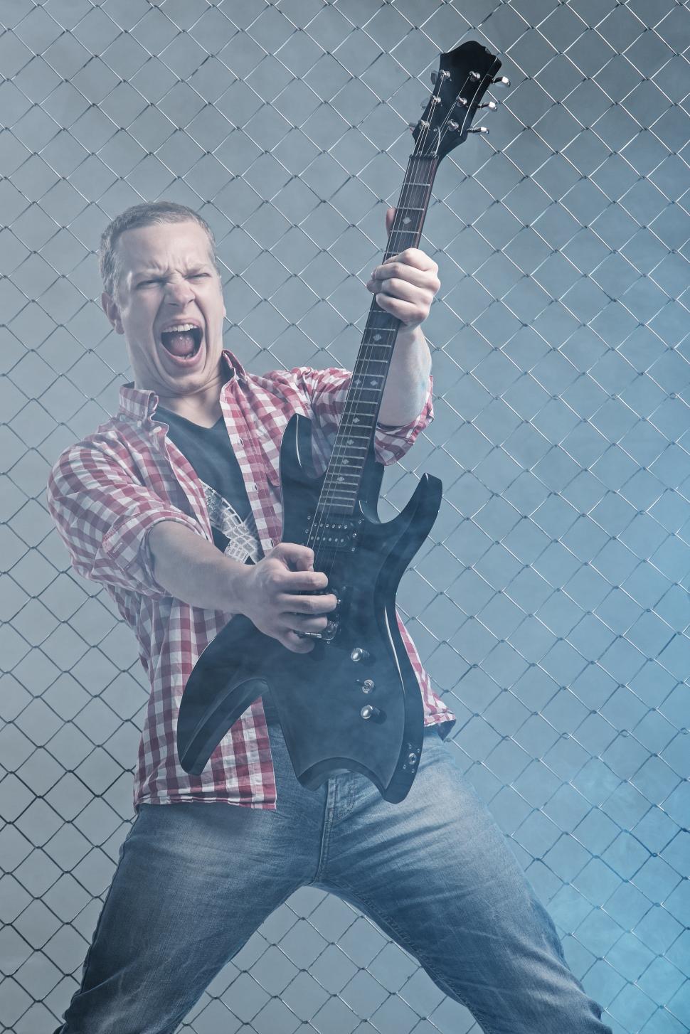 Free Image of Music. Young musician with a guitar on fence background 