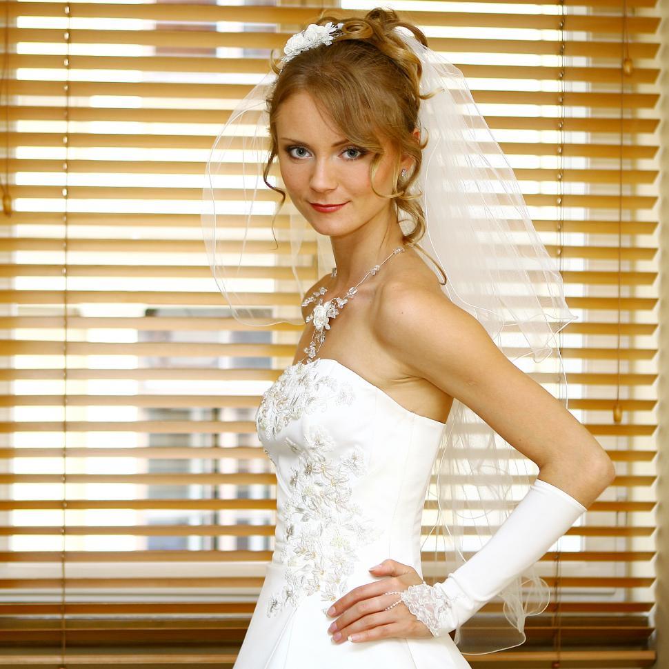 Free Image of bride looking at camera, standing in front of window 