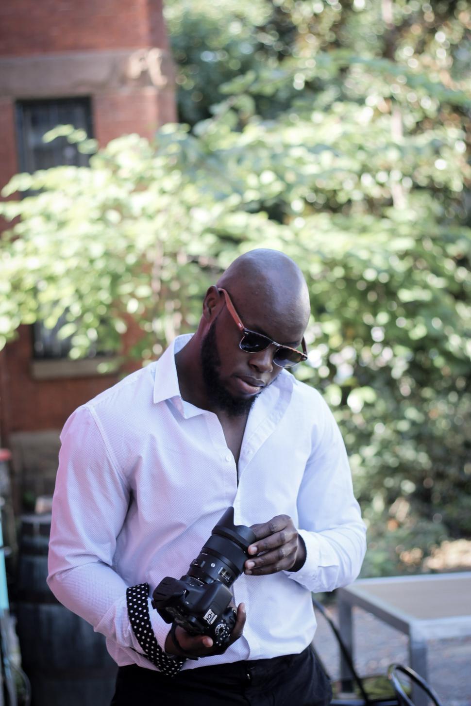 Free Image of Young Bald Man in white shirt holding DSLR camera 