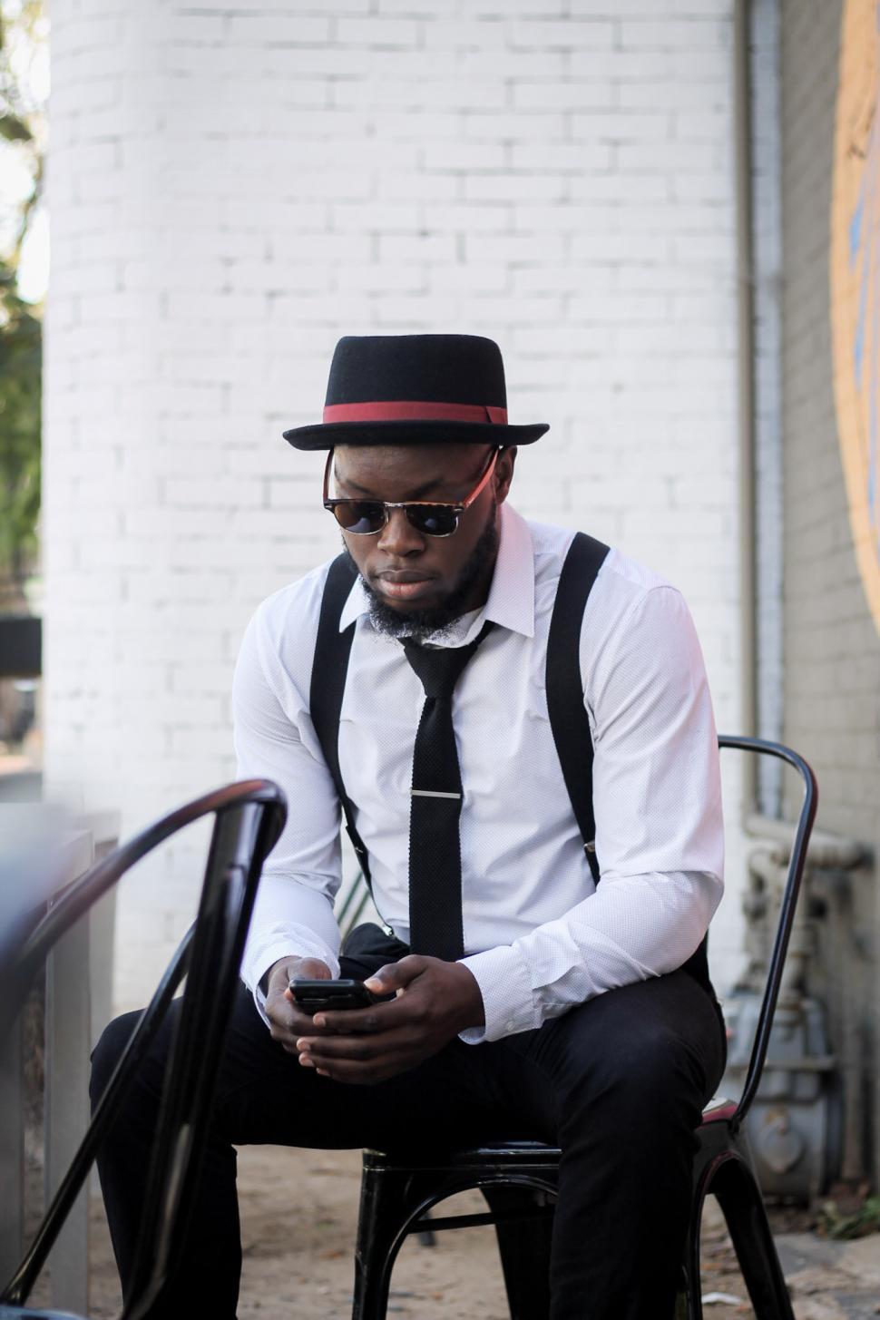 Free Image of Young Man in hat and suspenders using mobile phone 