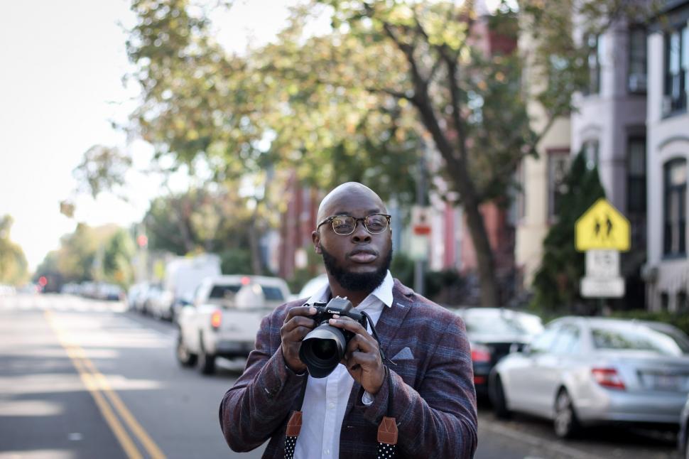 Free Image of Young photographer in glasses holding DSLR camera on the street 
