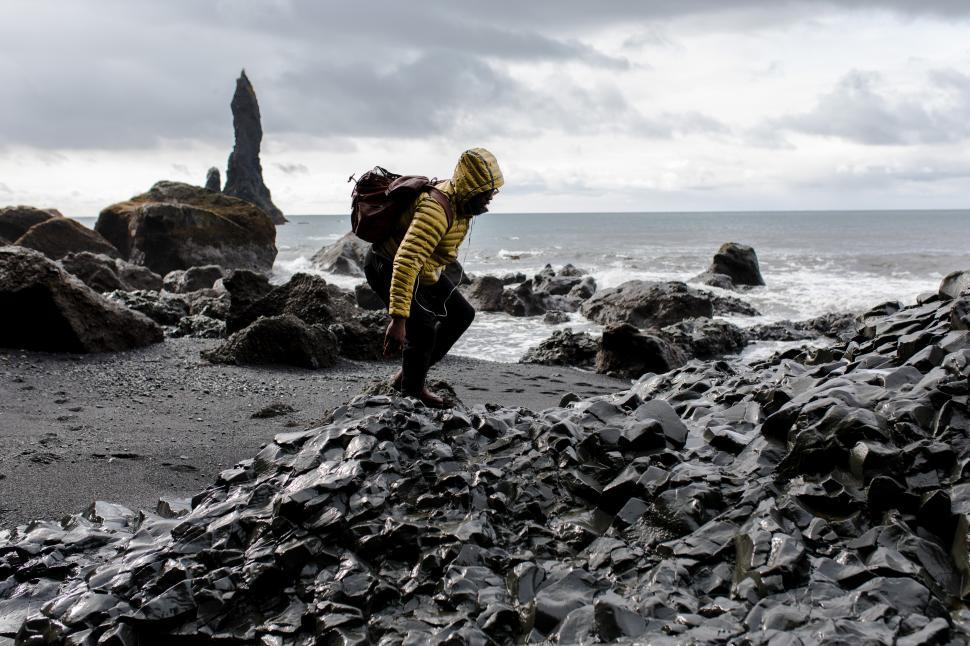 Free Image of Young Male Backpacker walking in Rain at seashore with rock mountains 
