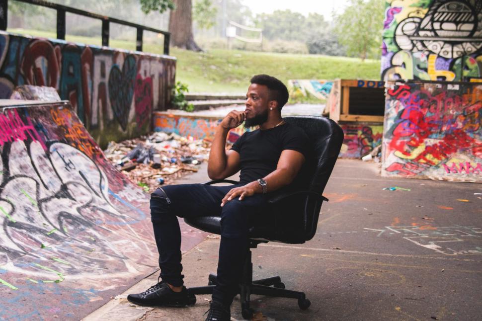 Free Image of Young Man in black t-shirt sitting on chair with graffiti walls 