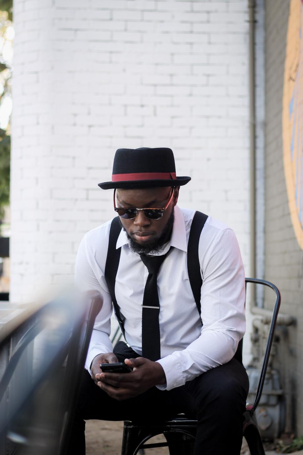 Free Image of Young Man wearing tie and suspenders using cell phone 