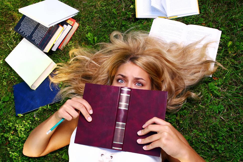 Download Free Stock Photo of Overworked young student hiding behind open book 