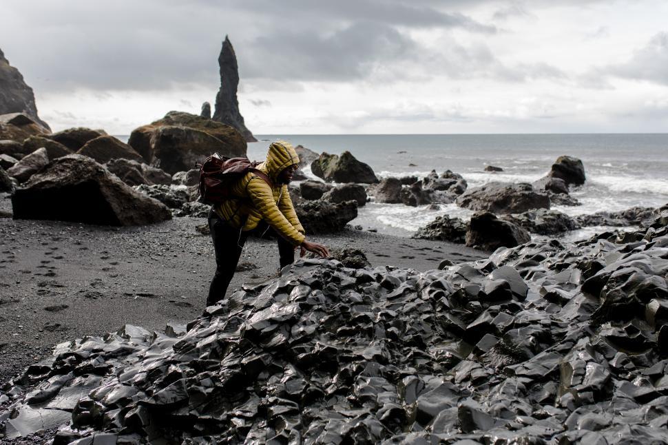 Free Image of Young Male with leather backpack at seashore with rock mountains 