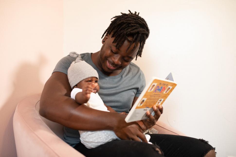 Free Image of Young Smiling Father With Newborn Baby Sitting on Sofa Chair 
