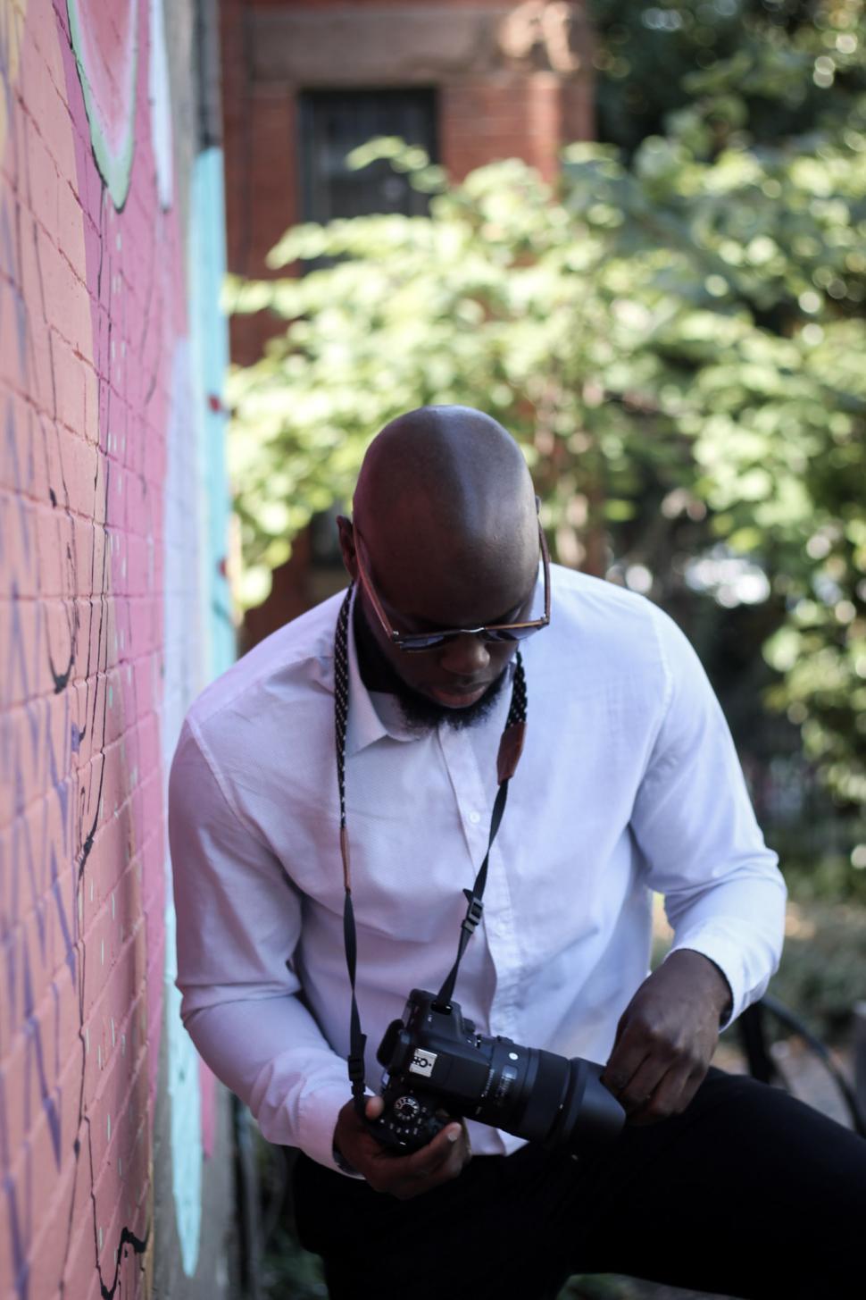 Free Image of Young Man with shaved head, in white shirt holding professional camera - look 