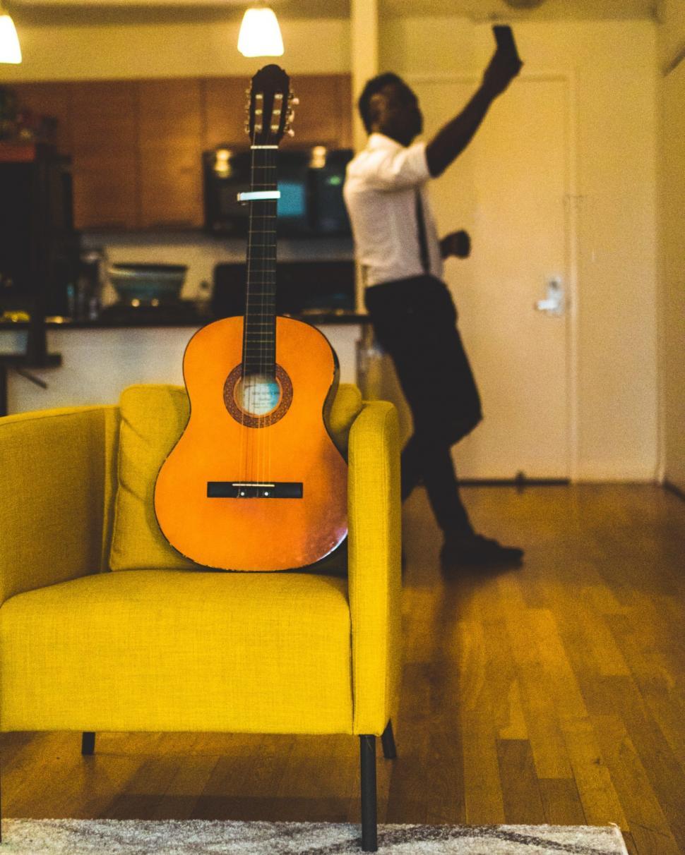 Free Image of Acoustic Guitar on Sofa Chair With young man taking picture with 