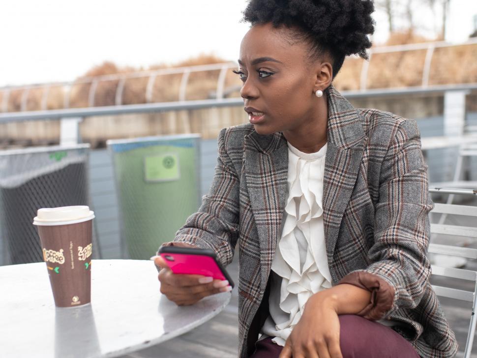 Free Image of Young well dressed woman in tweed blazer holding smartphone - looking aw 