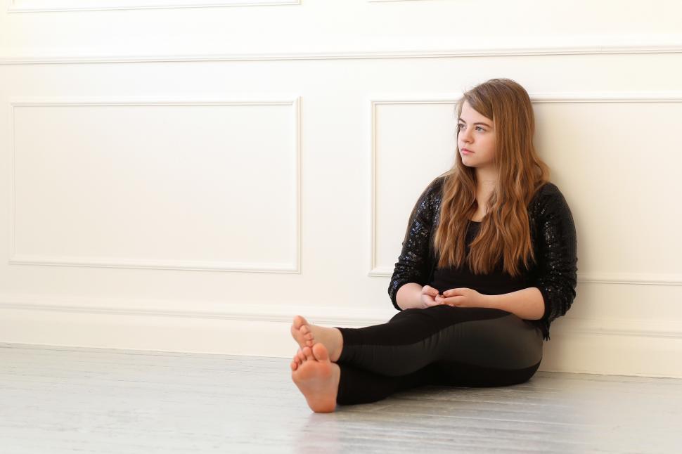 Free Image of Teenage sitting on the floor against a wall 