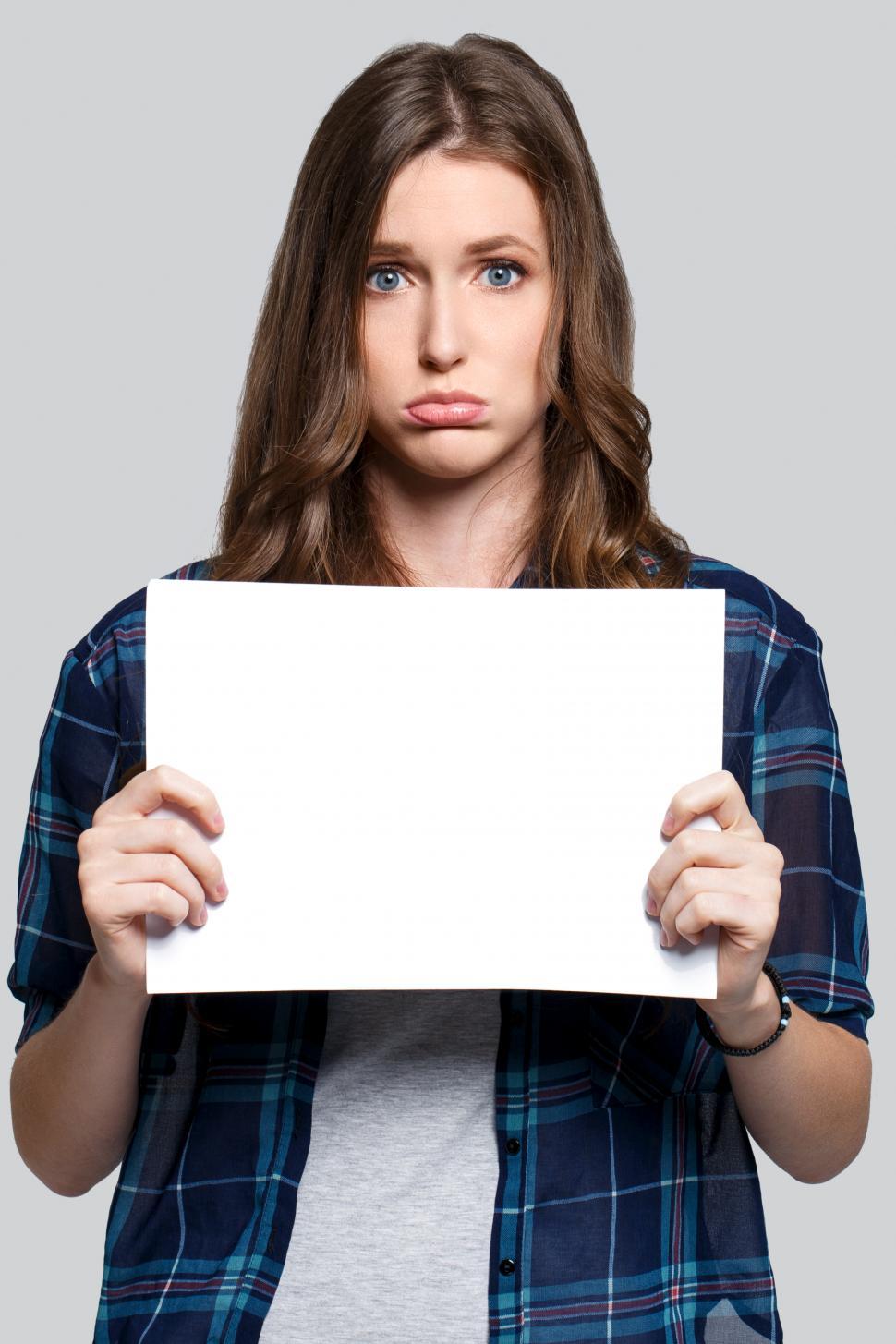 Free Image of Girl holding blank white card, looking concerned 