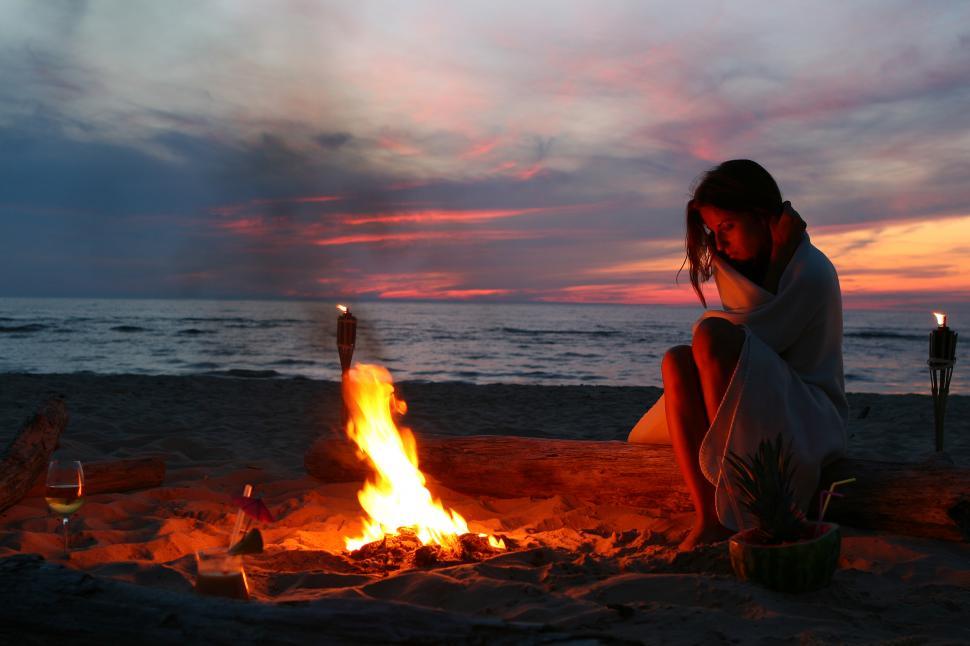 Download Free Stock Photo of Young woman sitting by fire at the beach 