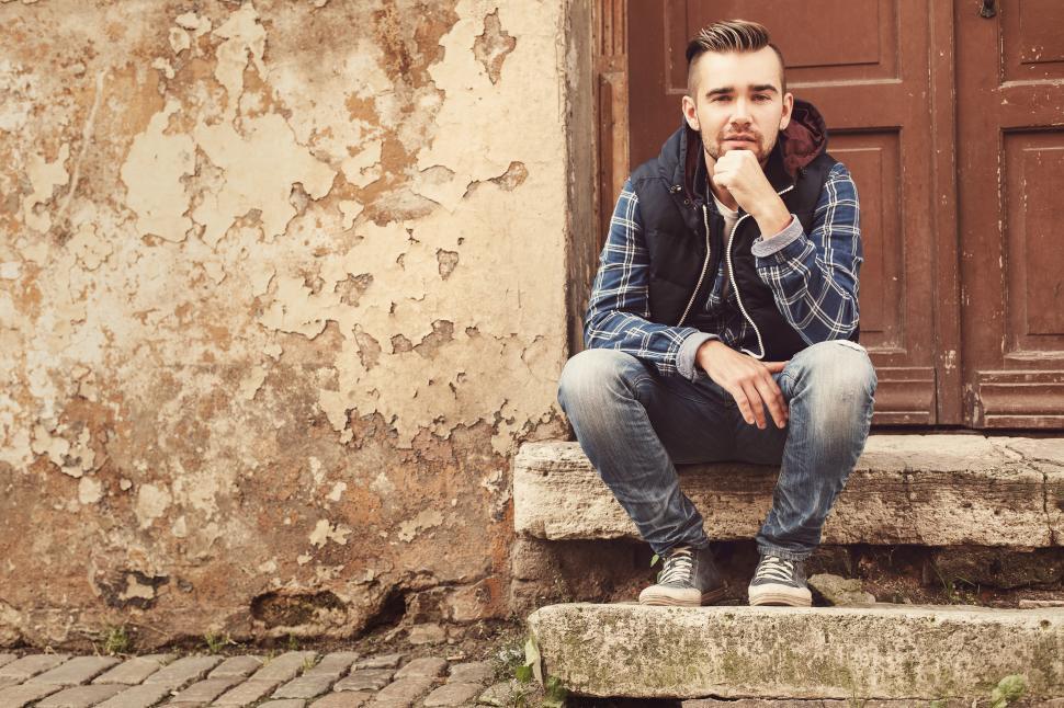 Free Image of Young man outdoors sitting on a stoop on the street 