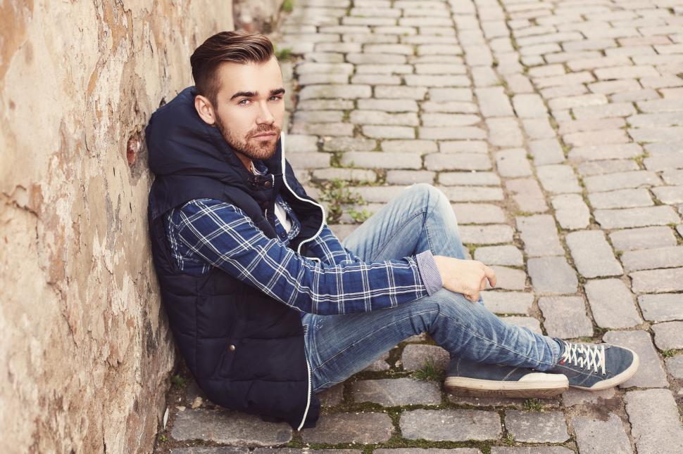 Free Image of Young man sitting against a masonry wall 