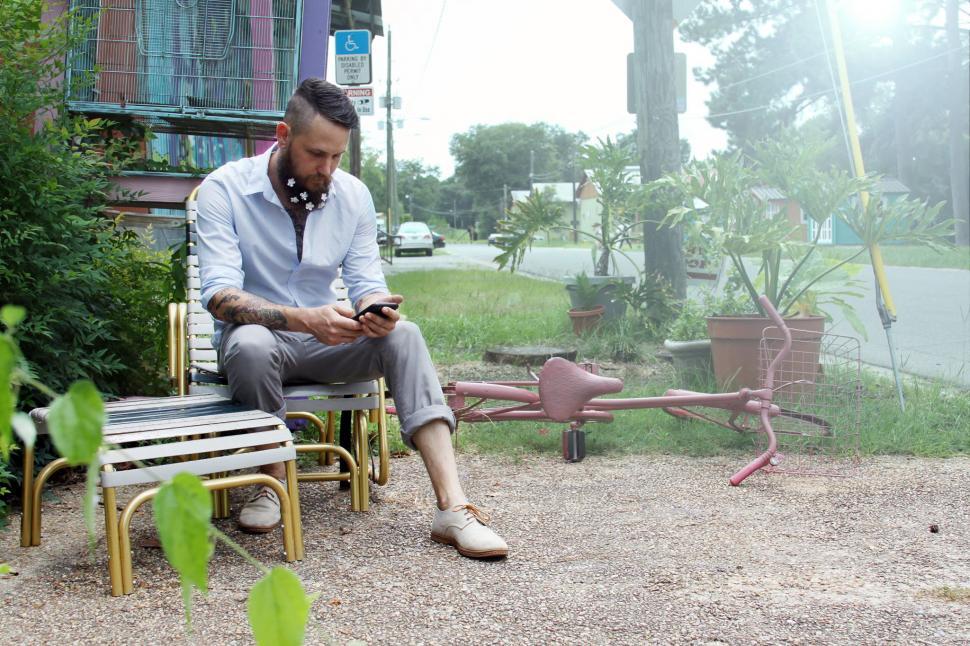 Free Image of Urban man with flowers on beard using cell phone on park bench 