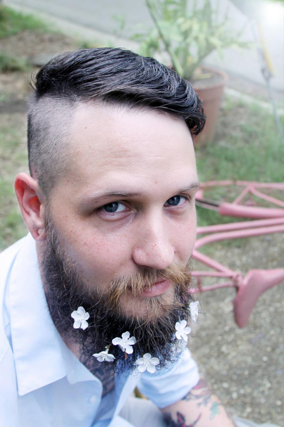 Free Image of Urban man with flowers on beard sitting in the park 