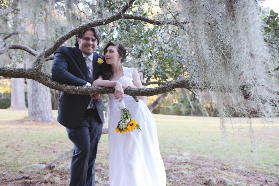 Free Image of Wedding couple under tree with sunflower bouquet 