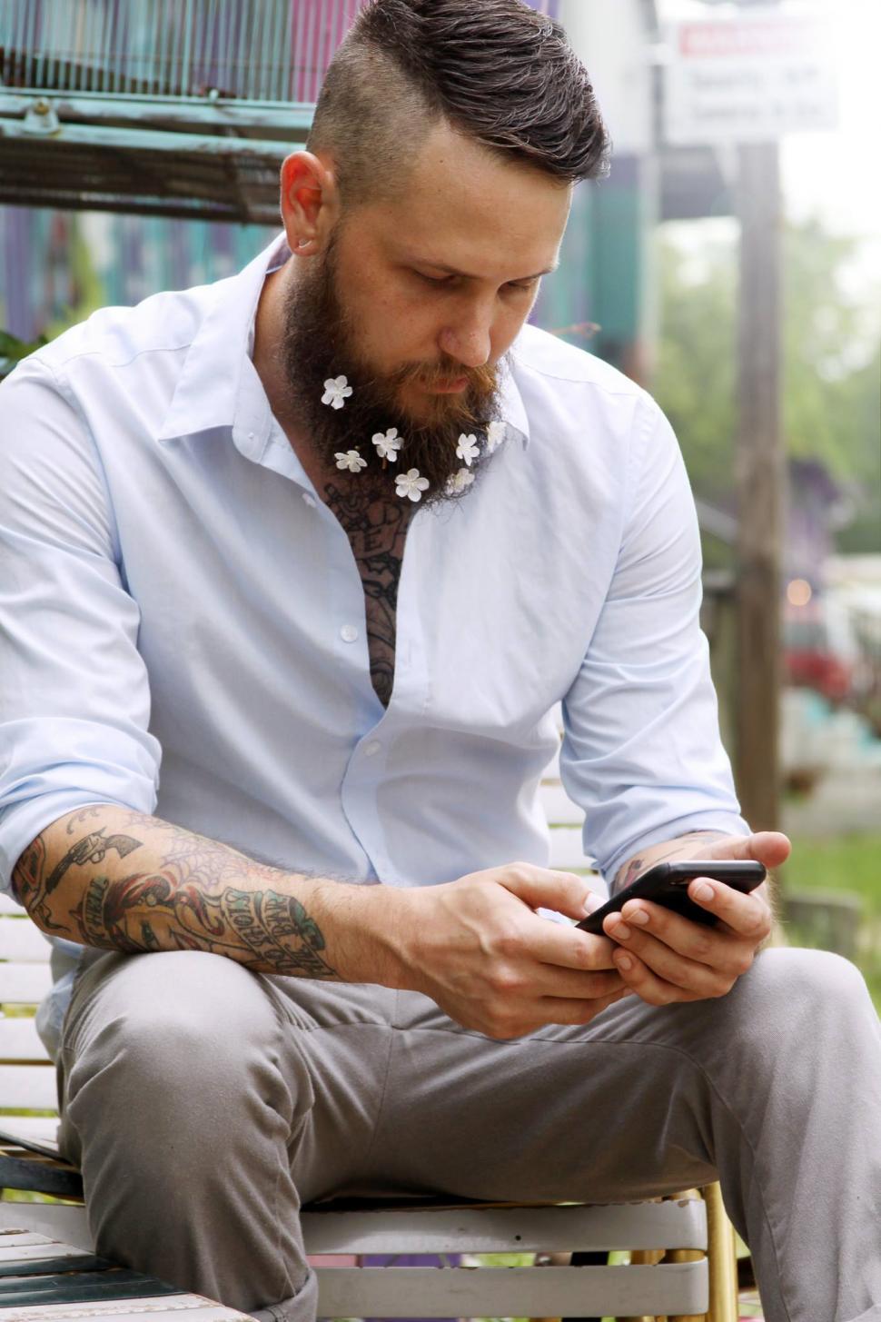 Free Image of Urban man with flowers on beard using cell phone 