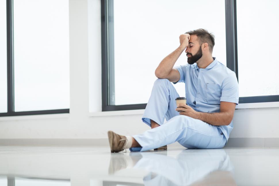 Free Image of Male nurse with upset expression sitting on the ground - hand on 