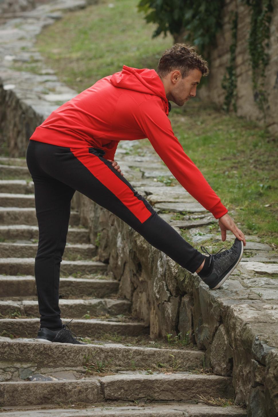 Free Image of Male runner in red jacket doing leg stretching exercise 