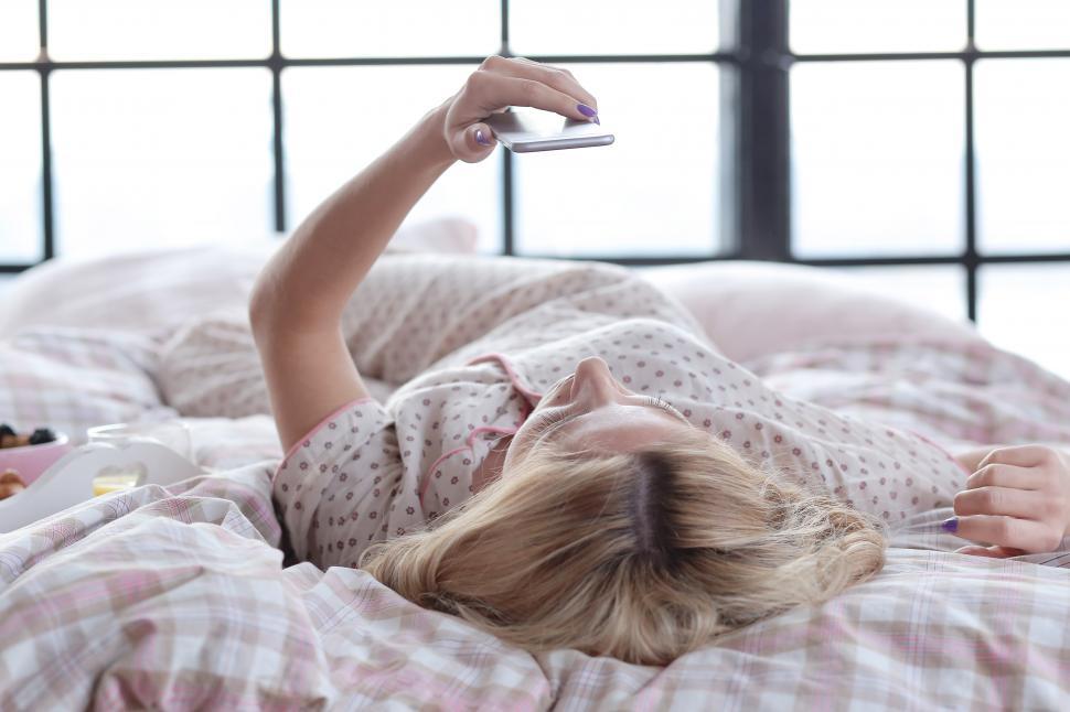 Free Image of Girl in bed, looking at her phone 