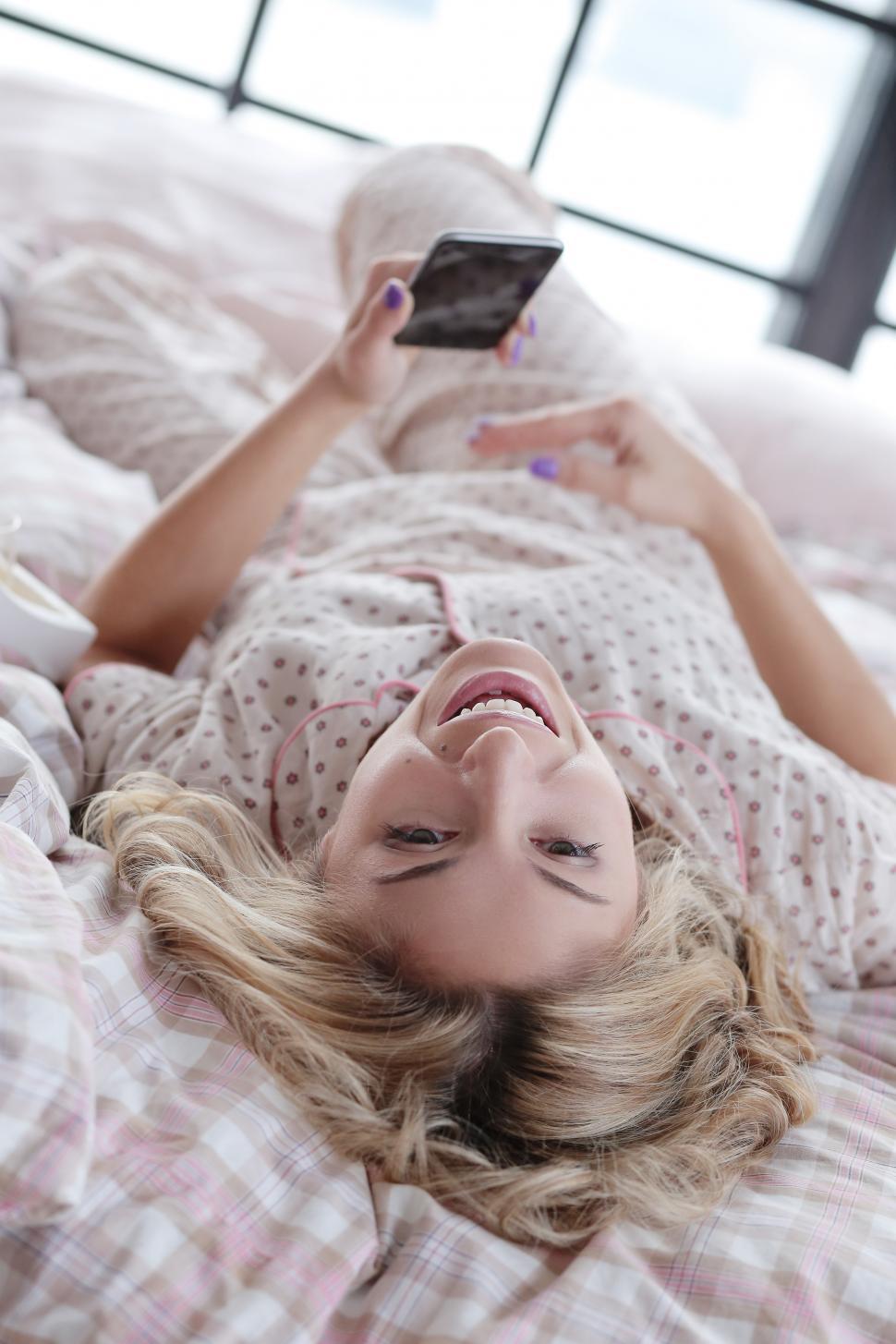 Free Image of Girl in bed, laughing at something on her phone 