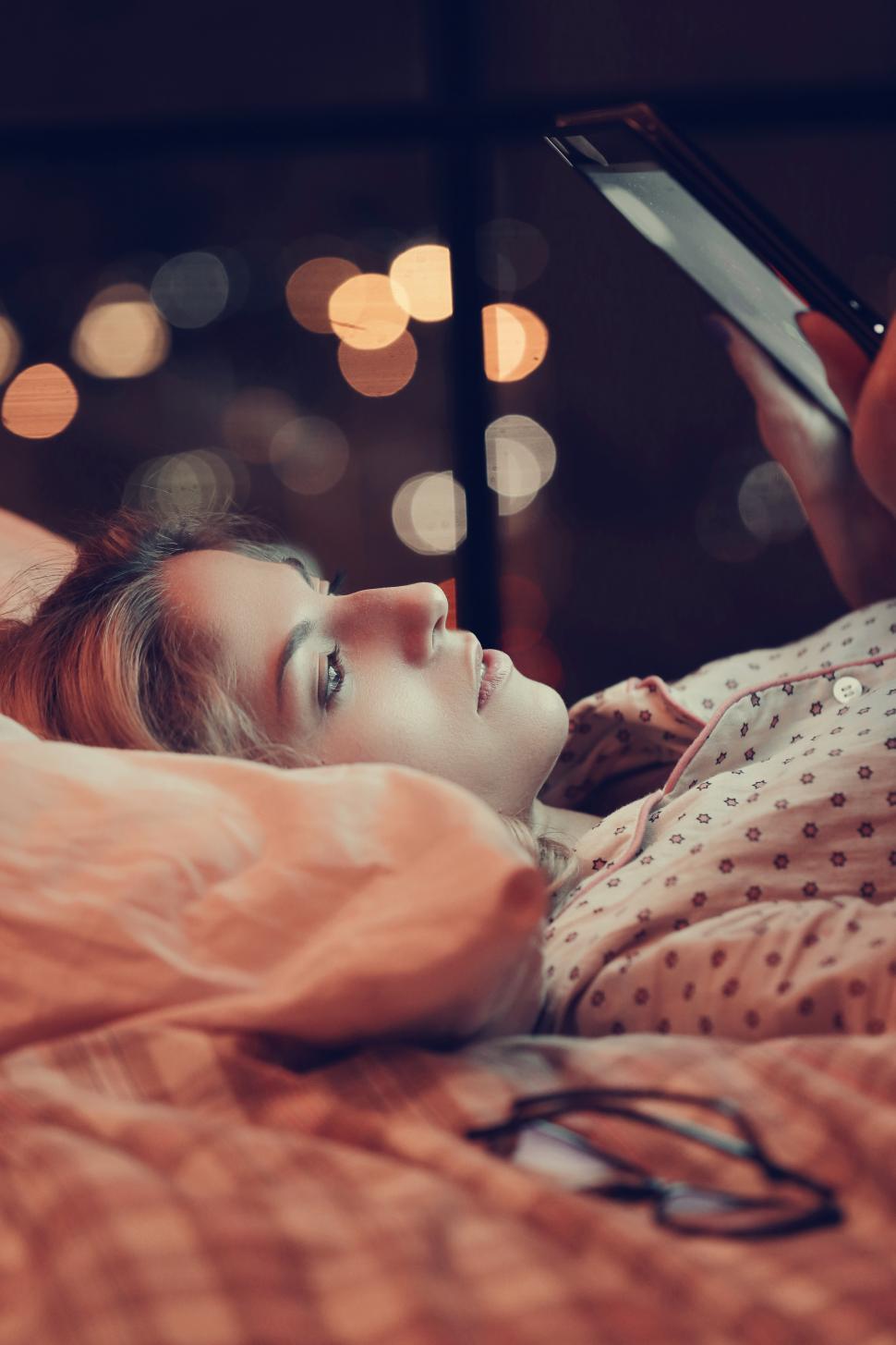 Free Image of Girl in bed reading from a tablet 