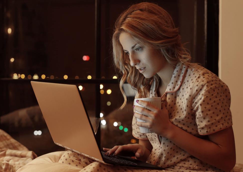 Free Image of Woman with a mug, working on her laptop, softly illuminated  