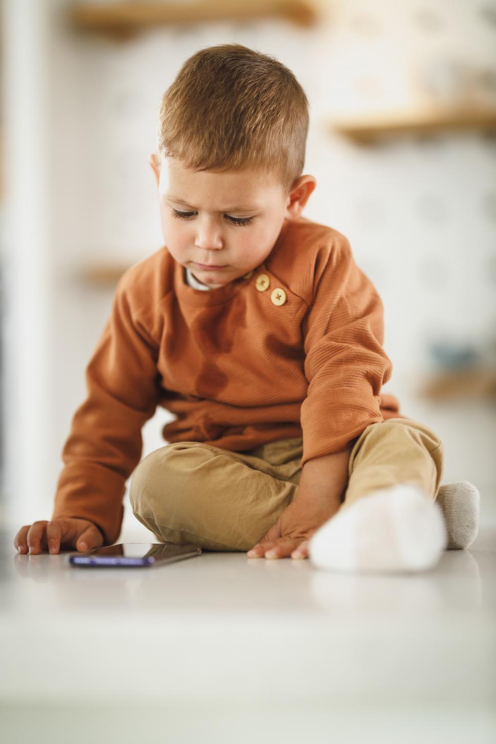 Free Image of Toddler boy with mobile phone sitting on the floor 