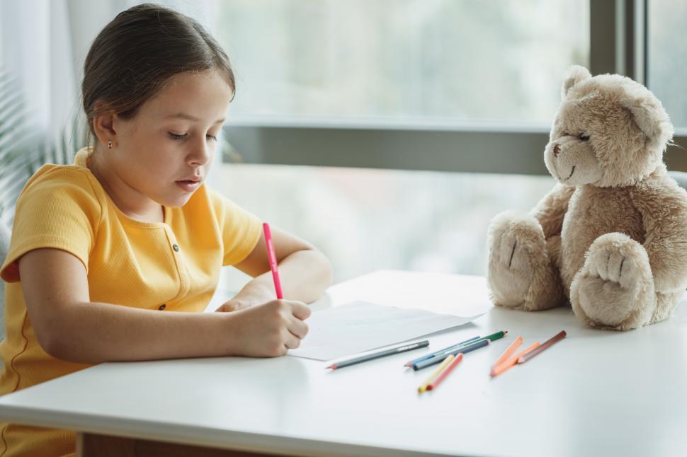 Free Image of Little girl doing homework with a teddy bear 