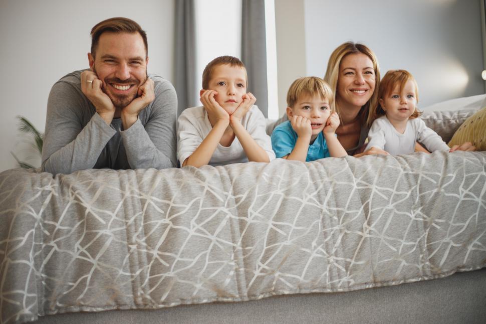 Free Image of Cheerful Caucasian family lying on bed - looking at camera 