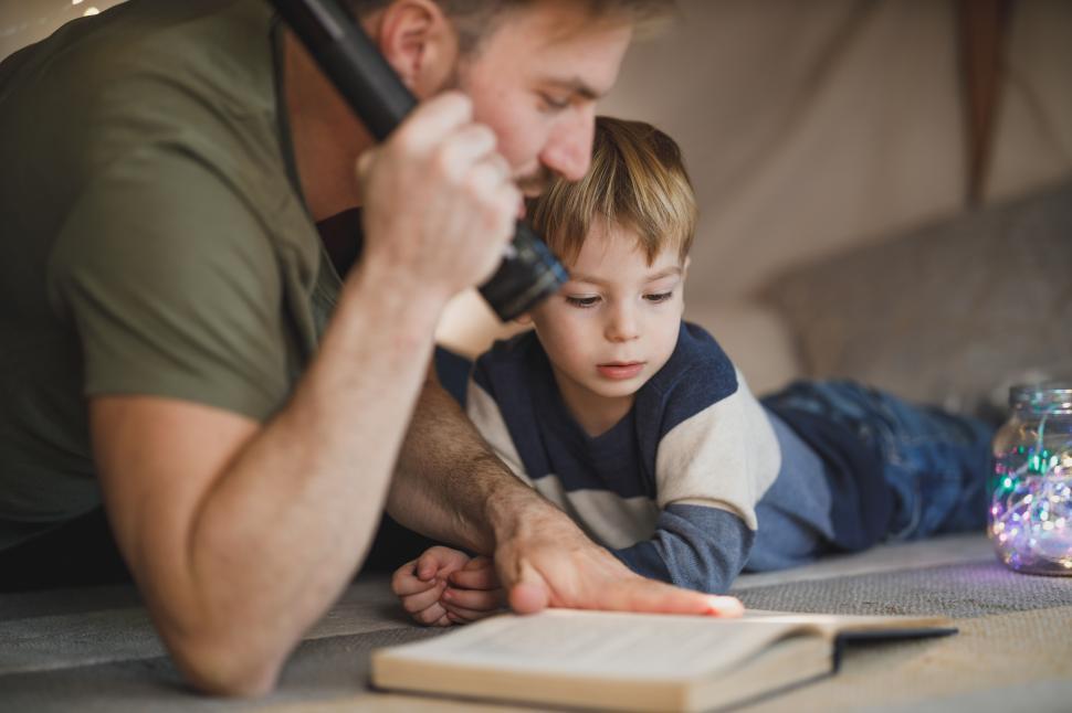 Free Image of Happy father and son reading book with a flashlight in a tent at night 
