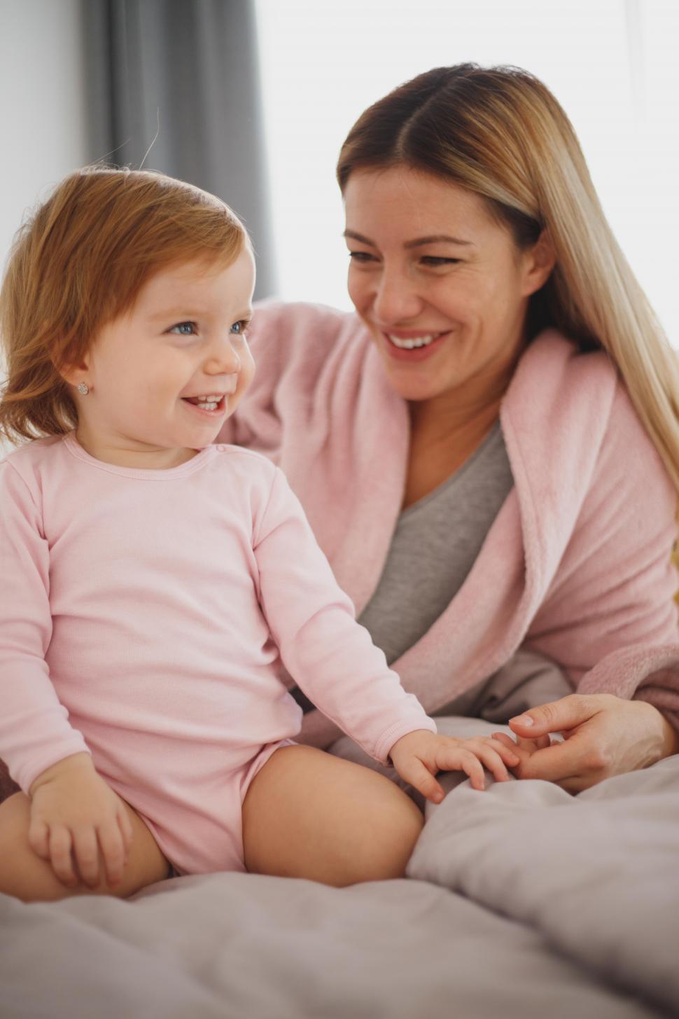 Free Image of Happy mother with her toddler daughter sitting on bed 