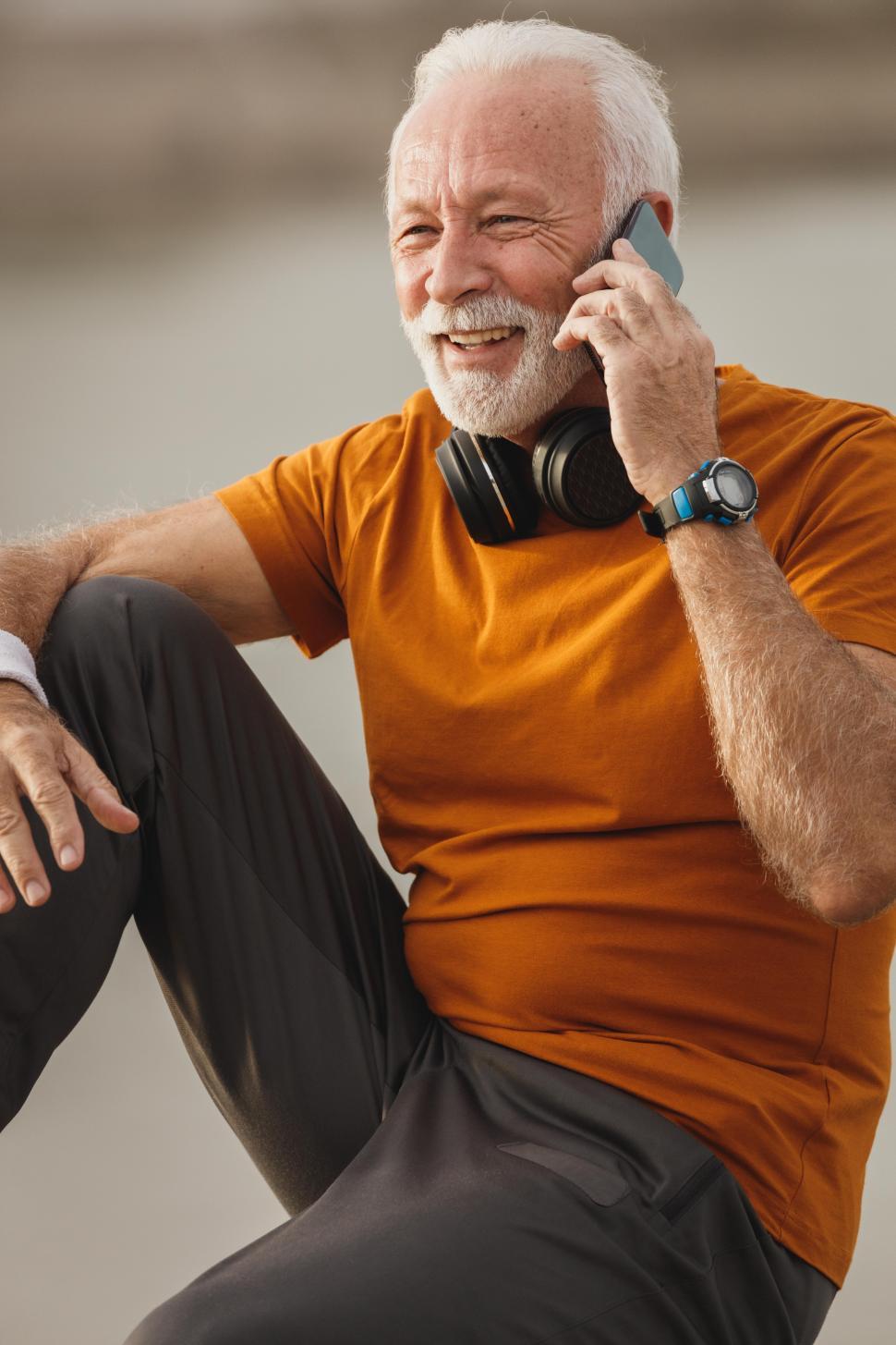 Free Image of Senior man with headphones on neck talking on mobile phone 