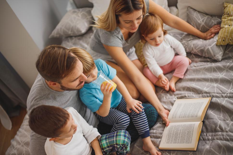 Free Image of Young parents and kids reading a book in bed 