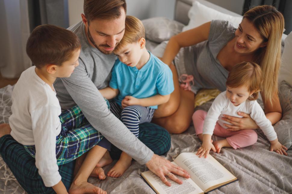 Free Image of Young parents and kids with book in family bed 