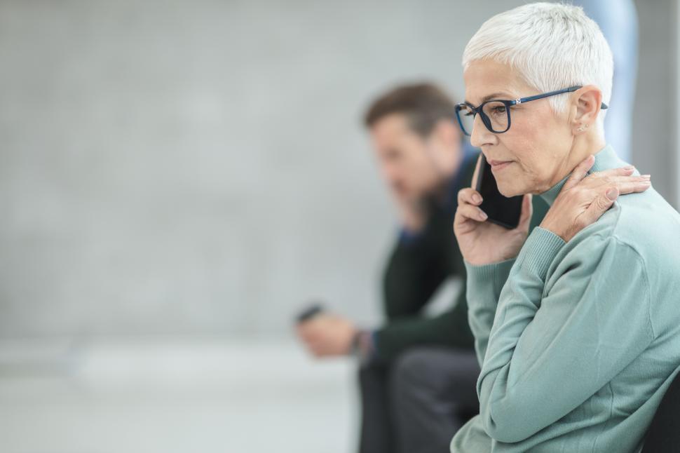 Free Image of Elderly Woman talking on phone while sitting and waiting at the 