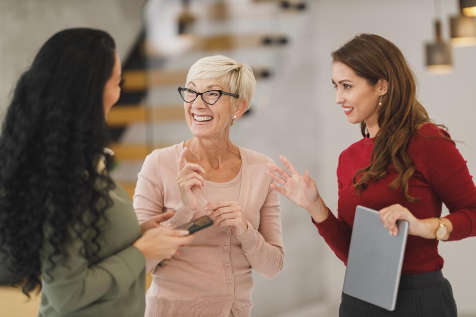 Free Image of Three female coworkers talking and smiling while standing in the 