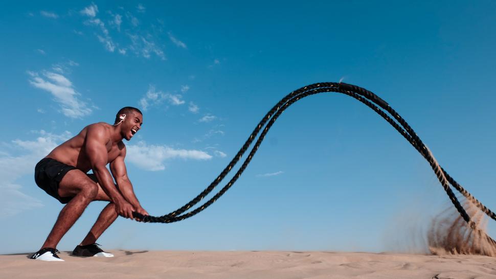 Free Image of Young muscular shirtless man exercising with rope in desert 