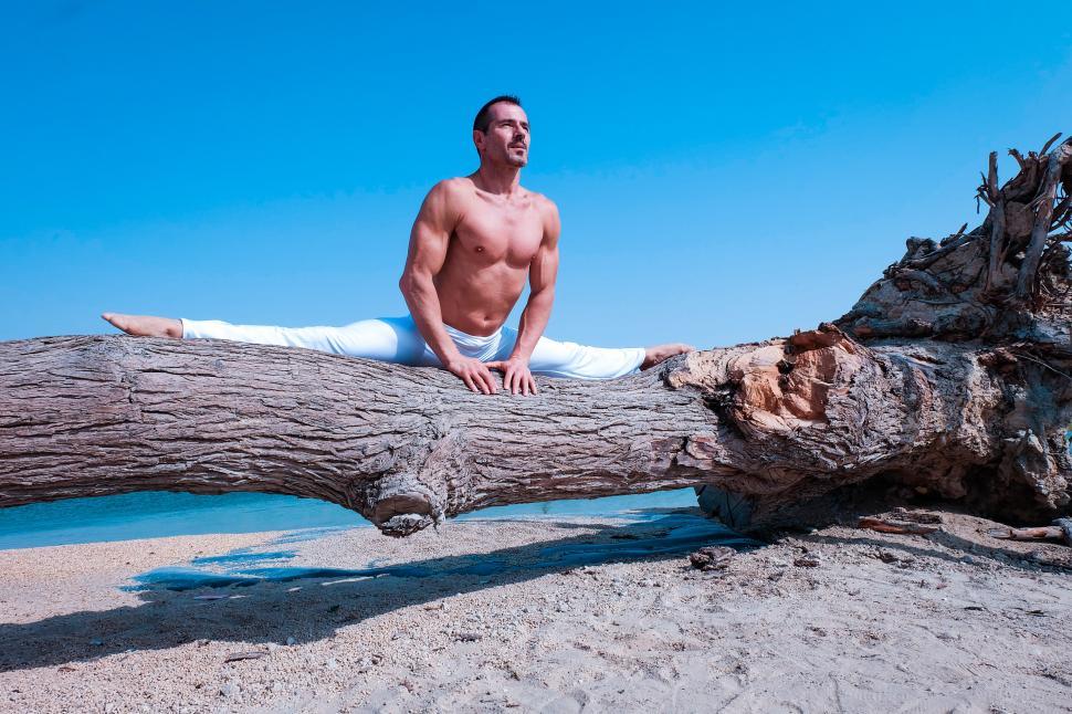 Free Image of Muscular man doing leg splits stretch on driftwood 