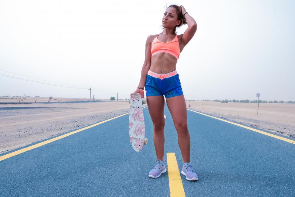 Free Image of Female athlete standing and holding skateboard on road 