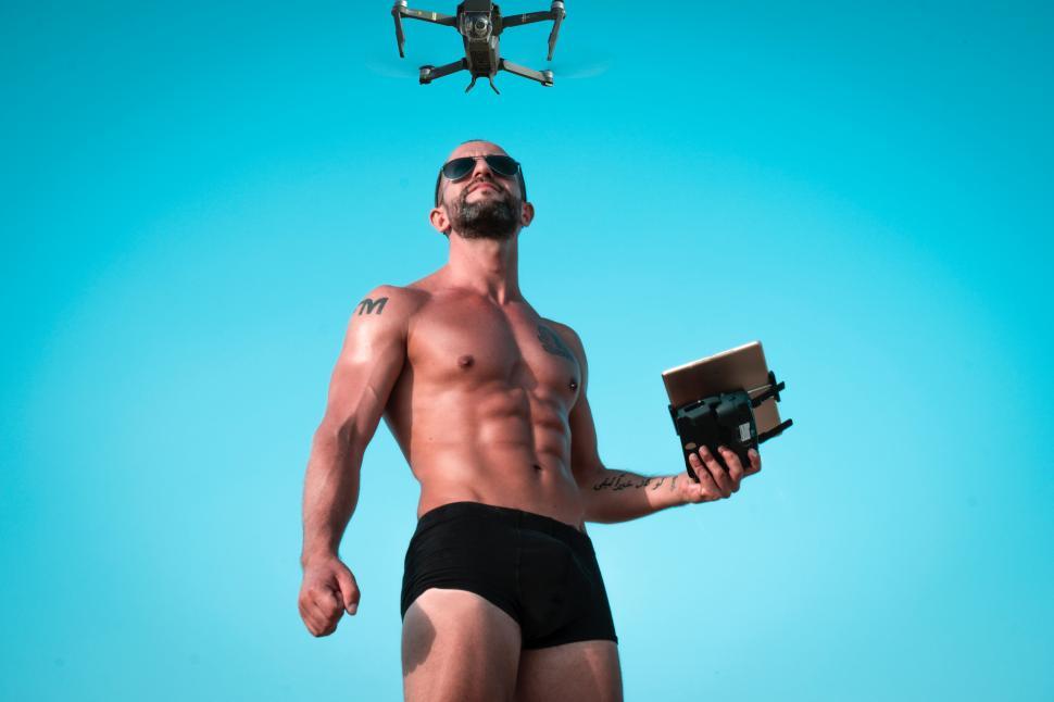 Free Image of Shirtless man in sunglasses with remote control of drone camera 