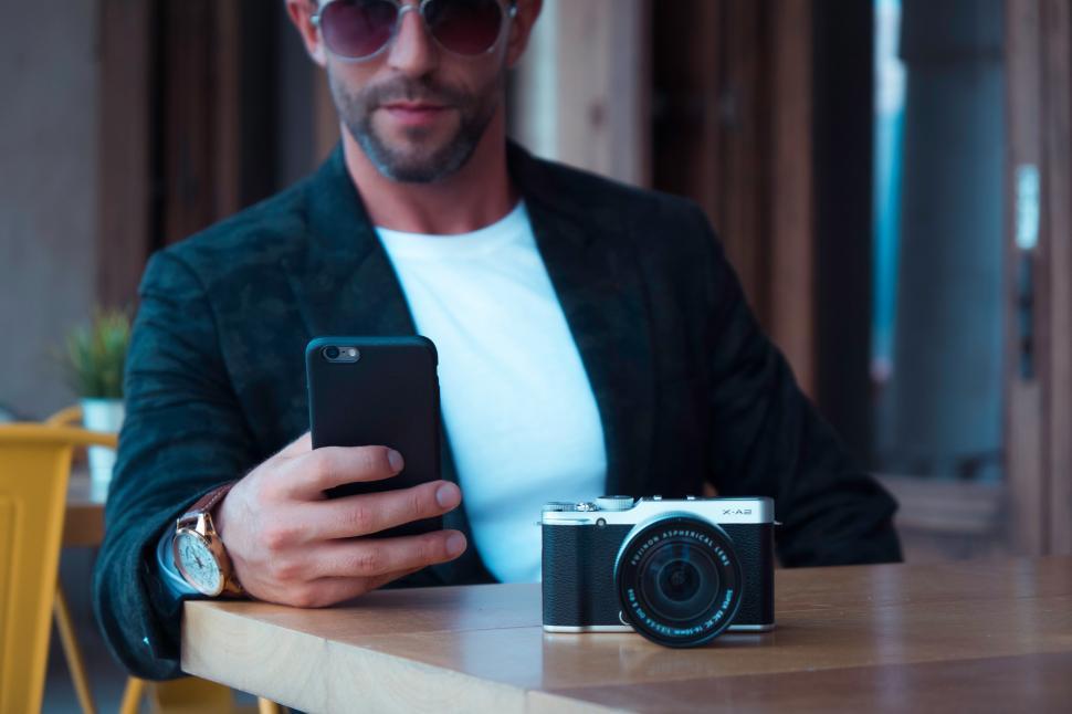 Free Image of Young male in sunglasses with mobile phone and camera sitting in 