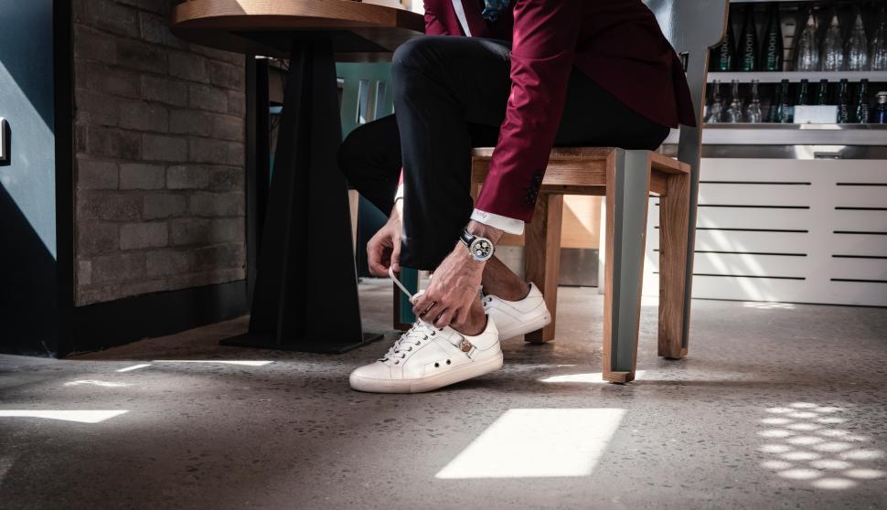 Free Image of Man sitting on bar stool and tying shoelaces of white sneakers 